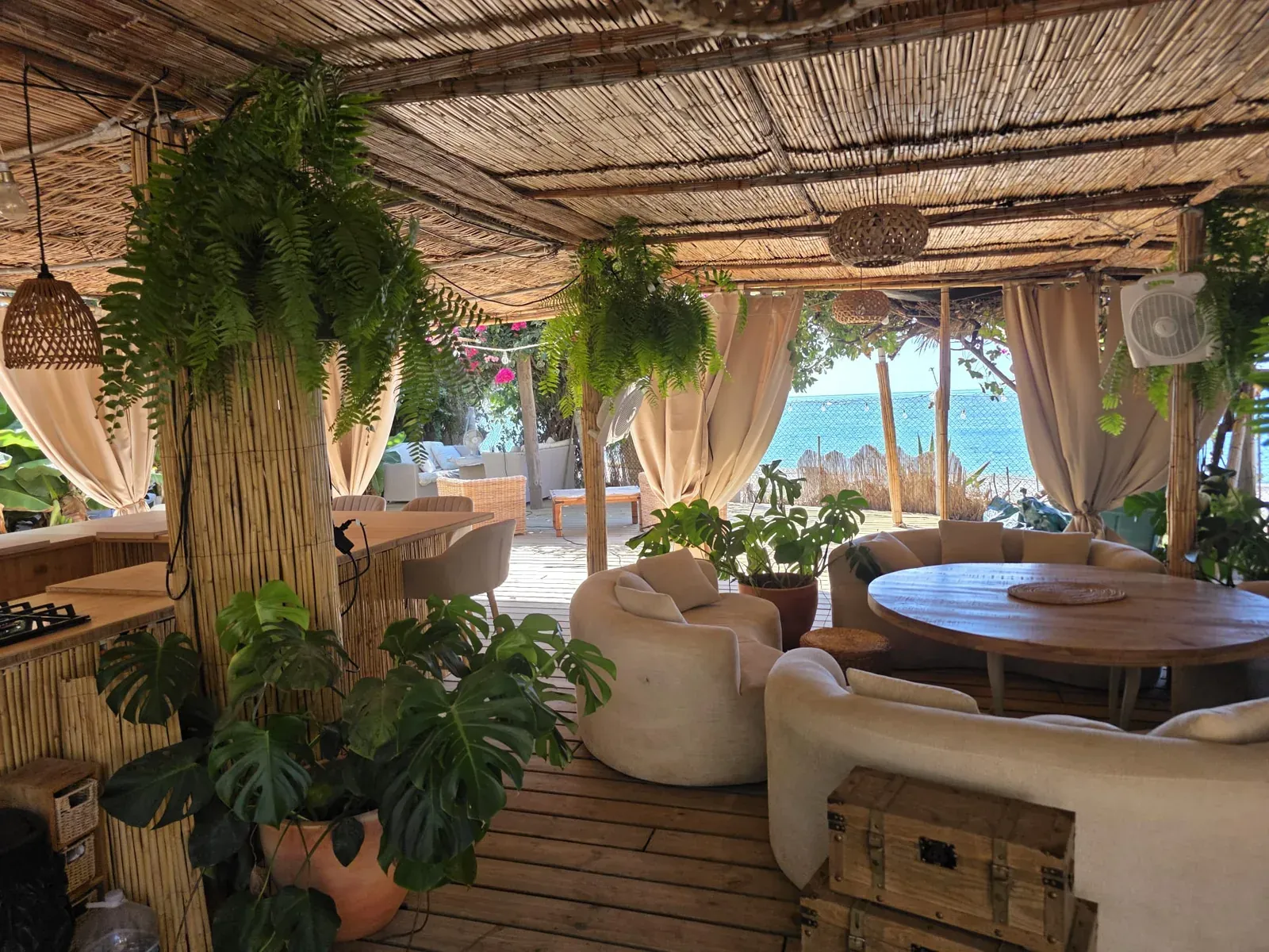 Salon couvert de La Plage avec canapés ronds et grande table, ouvert sur la mer